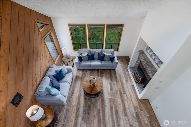 living room with a textured ceiling, wooden walls, a fireplace, and wood finished floors