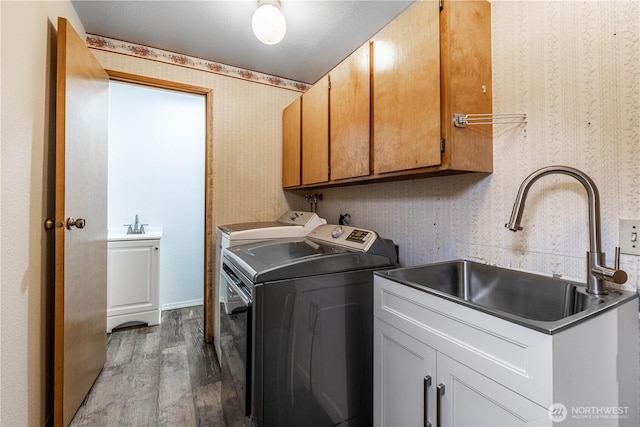 washroom with wallpapered walls, cabinet space, wood finished floors, independent washer and dryer, and a sink