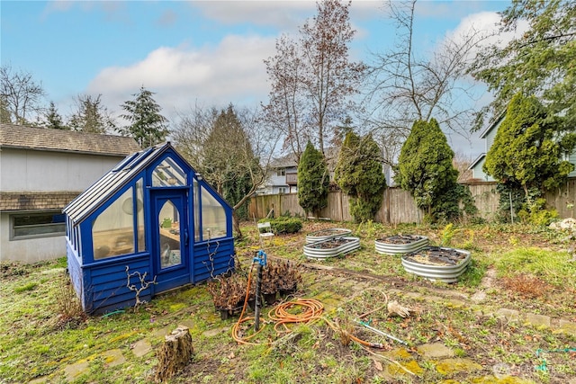 view of home's exterior featuring an outbuilding, a greenhouse, fence, and a vegetable garden