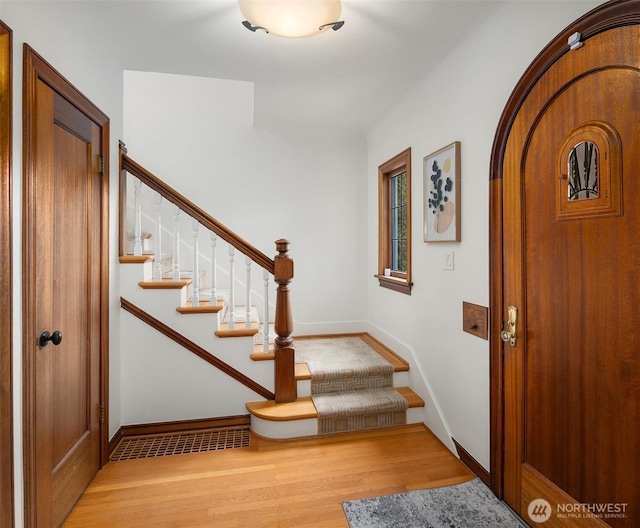 entryway with arched walkways, stairway, baseboards, and wood finished floors