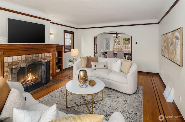 living room with arched walkways, a fireplace, crown molding, and wood finished floors