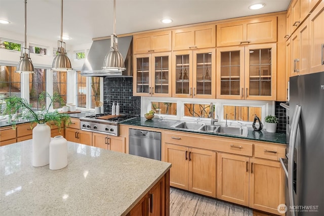 kitchen featuring a sink, glass insert cabinets, appliances with stainless steel finishes, wall chimney range hood, and decorative backsplash