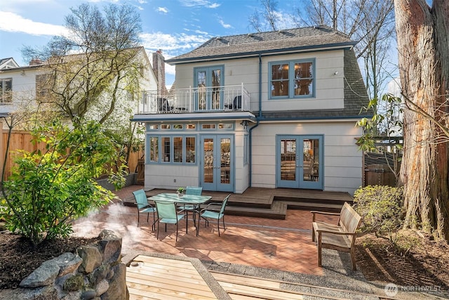 back of property with fence, french doors, outdoor dining area, a balcony, and a patio area