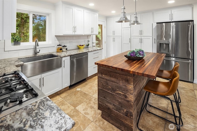 kitchen with light stone counters, decorative backsplash, stainless steel appliances, white cabinetry, and a sink