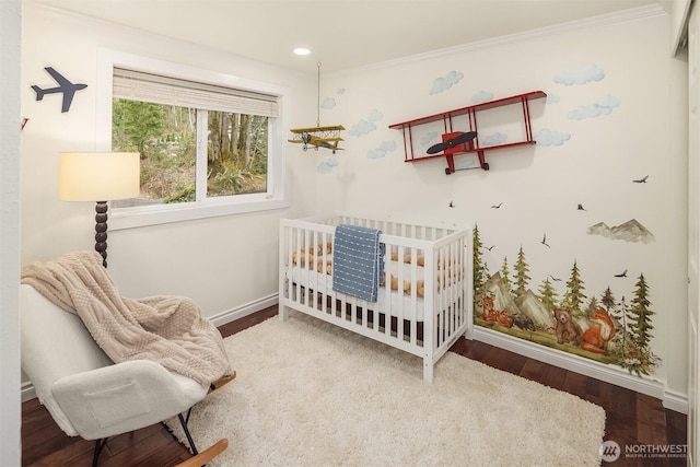 bedroom featuring wood finished floors, recessed lighting, a nursery area, crown molding, and baseboards