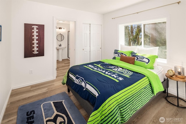 bedroom with ensuite bath, wood finished floors, baseboards, and a closet