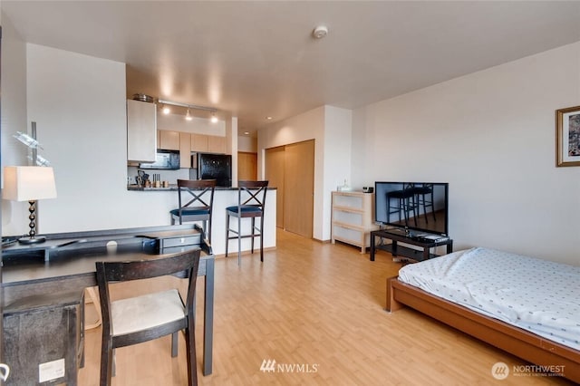 bedroom with black fridge and light wood-style flooring