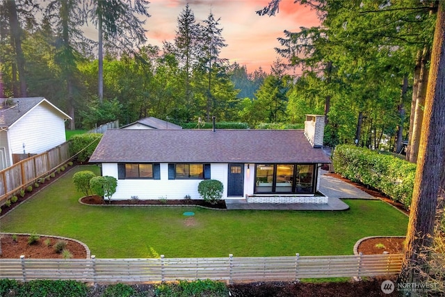 view of front of house featuring a front lawn, fence private yard, roof with shingles, and a chimney