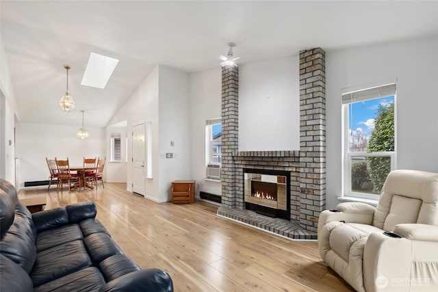 living area with cooling unit, a fireplace, light wood-style floors, vaulted ceiling with skylight, and baseboards