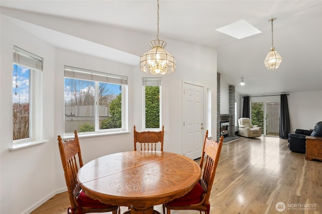 dining space featuring lofted ceiling with skylight, baseboards, a fireplace, and light wood finished floors