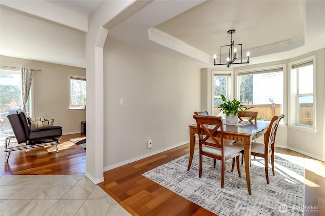 dining area with baseboards, ornamental molding, an inviting chandelier, a tray ceiling, and light wood-style floors