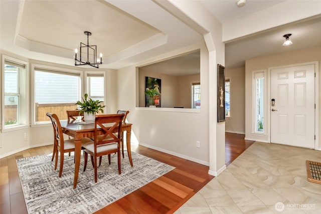 dining area with a raised ceiling, a notable chandelier, and wood finished floors