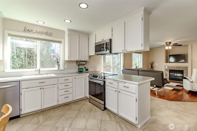 kitchen featuring white cabinets, a glass covered fireplace, appliances with stainless steel finishes, a peninsula, and a sink