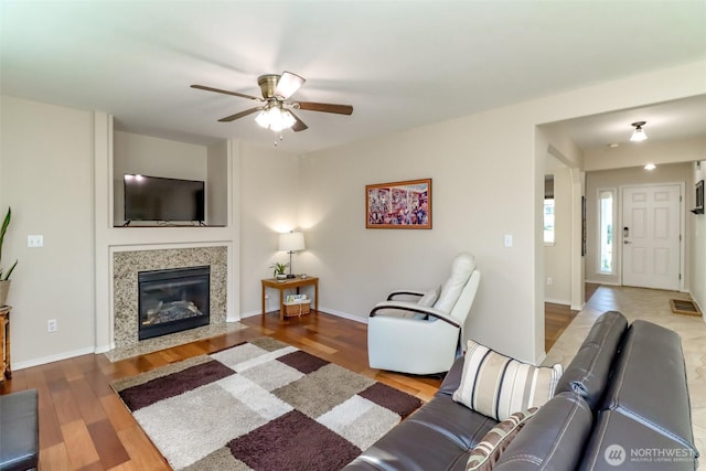 living room featuring ceiling fan, a fireplace, wood finished floors, and baseboards