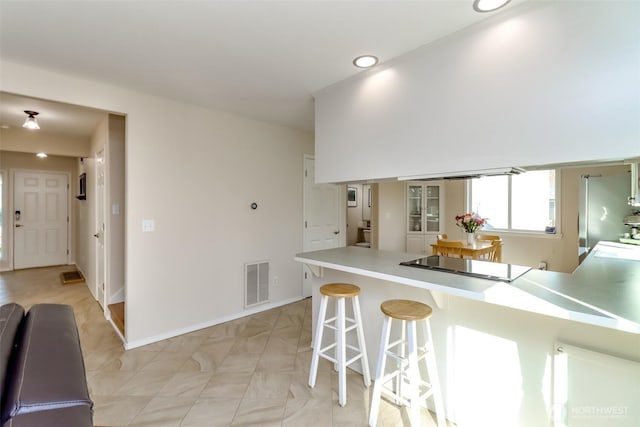 kitchen with a breakfast bar area, light countertops, visible vents, a peninsula, and baseboards