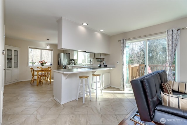 kitchen featuring a peninsula, a kitchen breakfast bar, light countertops, stainless steel refrigerator with ice dispenser, and decorative light fixtures