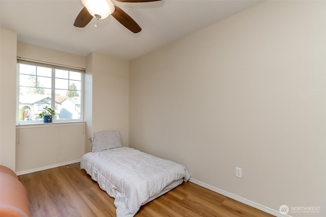 bedroom with a ceiling fan, visible vents, baseboards, and wood finished floors