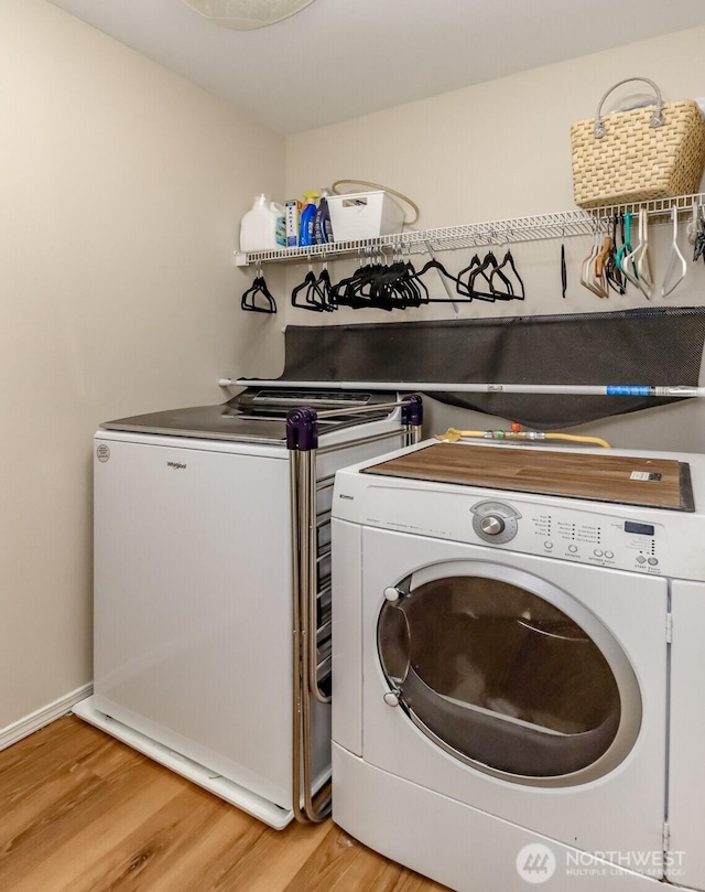 washroom with light wood-type flooring, laundry area, baseboards, and washing machine and clothes dryer