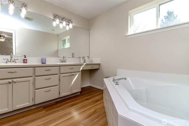 full bathroom with a sink, double vanity, wood finished floors, and a bath