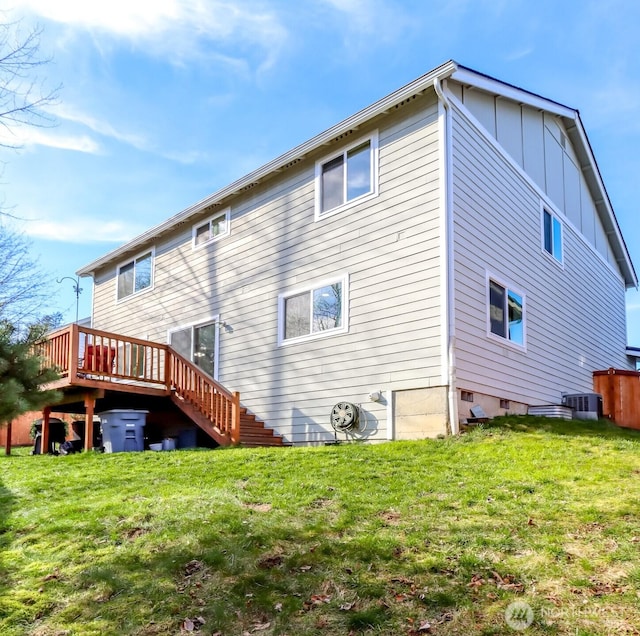 back of house with board and batten siding, central AC, and a yard