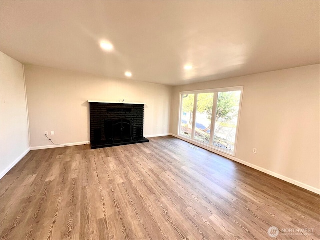 unfurnished living room featuring recessed lighting, a brick fireplace, baseboards, and wood finished floors