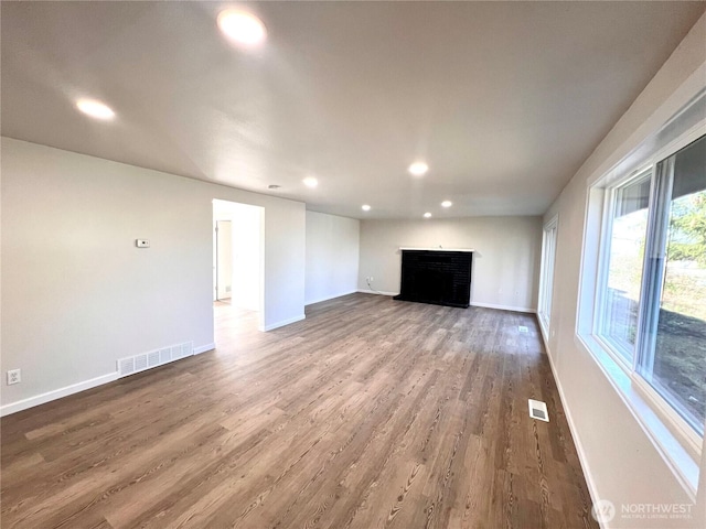 unfurnished living room with baseboards, visible vents, wood finished floors, a brick fireplace, and recessed lighting