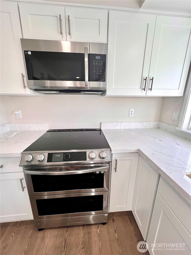 kitchen featuring appliances with stainless steel finishes, wood finished floors, light stone counters, and white cabinets