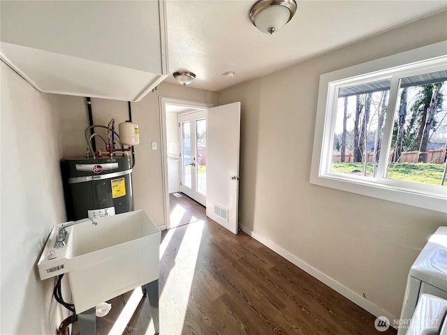 interior space with electric water heater, dark wood-type flooring, visible vents, baseboards, and washer / clothes dryer