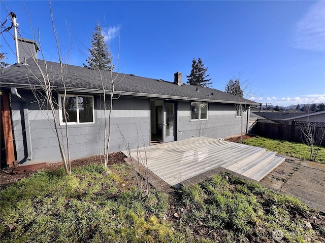 back of house featuring a shingled roof, fence, a chimney, and a wooden deck