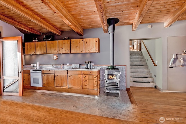 kitchen with wooden ceiling, light wood-style flooring, beamed ceiling, a wood stove, and light countertops