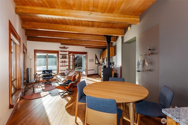 dining space with wooden ceiling, beamed ceiling, a wood stove, and light wood finished floors