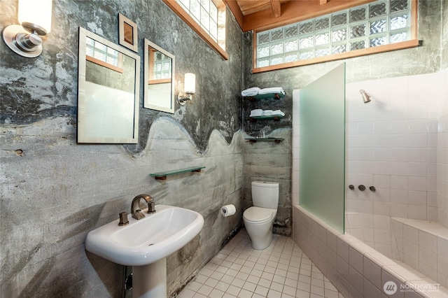 bathroom with tile patterned flooring, toilet, a sink, tile walls, and tiled shower / bath