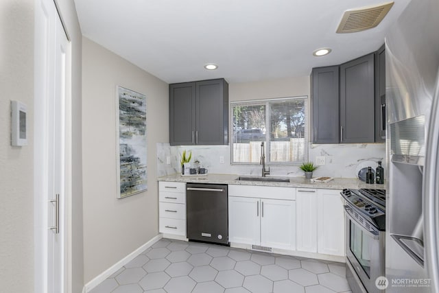 kitchen featuring visible vents, light stone counters, a sink, stainless steel appliances, and backsplash