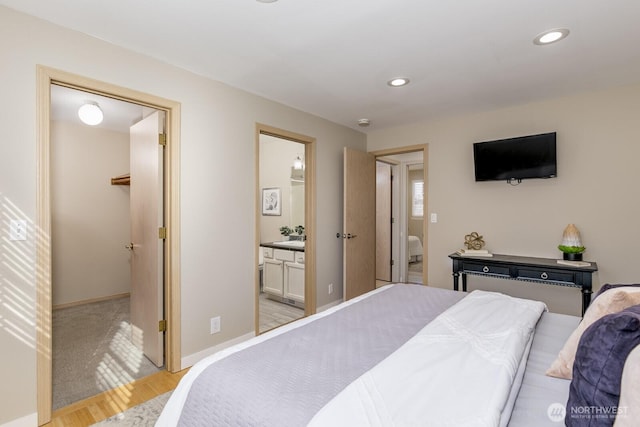 bedroom featuring baseboards, connected bathroom, light wood-style flooring, a spacious closet, and recessed lighting