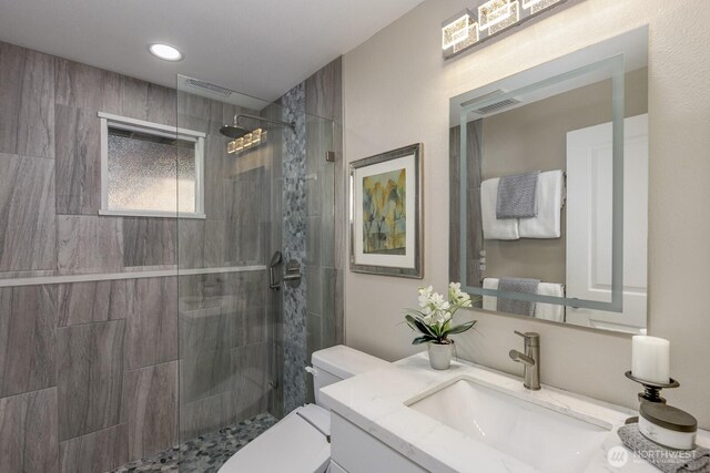 full bath with toilet, visible vents, a tile shower, and vanity