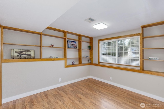 spare room featuring wood finished floors, visible vents, and baseboards