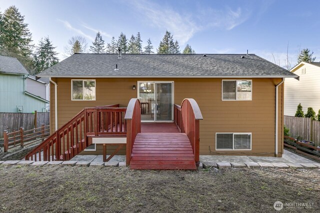 rear view of property with a shingled roof, fence, and a wooden deck