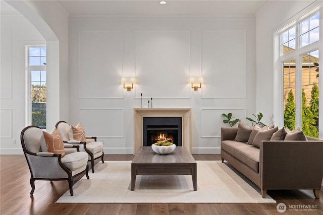 living area with a warm lit fireplace, arched walkways, a decorative wall, and crown molding