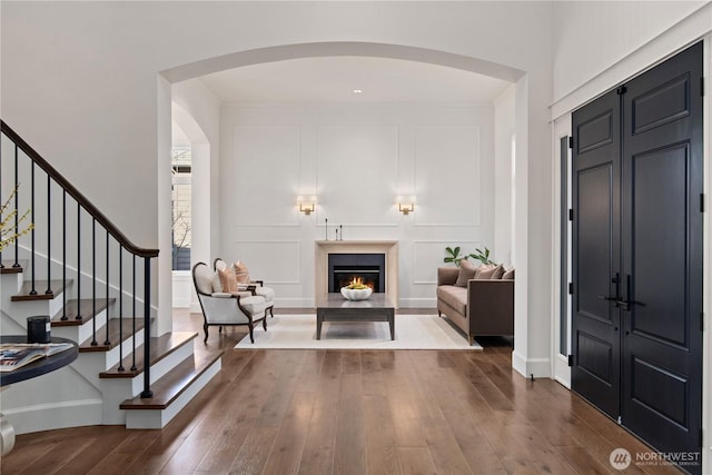 entryway with arched walkways, a decorative wall, a lit fireplace, stairway, and dark wood finished floors