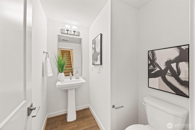 half bath with baseboards, toilet, and wood finished floors