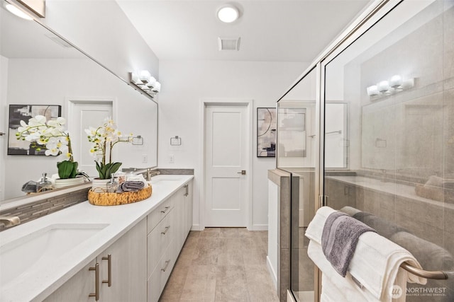 bathroom featuring double vanity, visible vents, a shower stall, and a sink