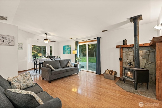 living area with visible vents, a wealth of natural light, light wood-style flooring, and a wood stove