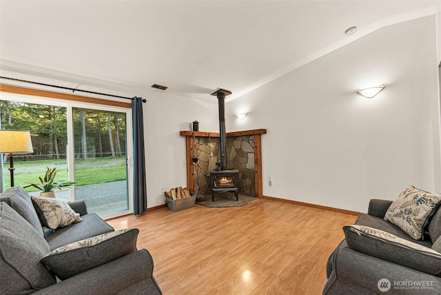 living area with visible vents, baseboards, vaulted ceiling, light wood-type flooring, and a wood stove