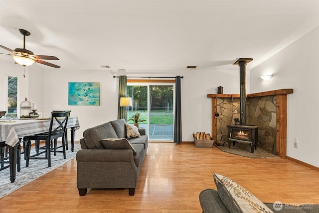 living room featuring a wood stove, ceiling fan, visible vents, and wood finished floors