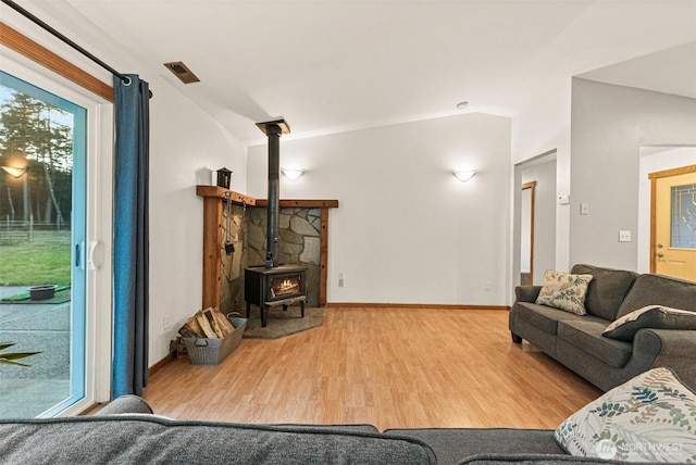 living room with lofted ceiling, a wood stove, baseboards, and wood finished floors