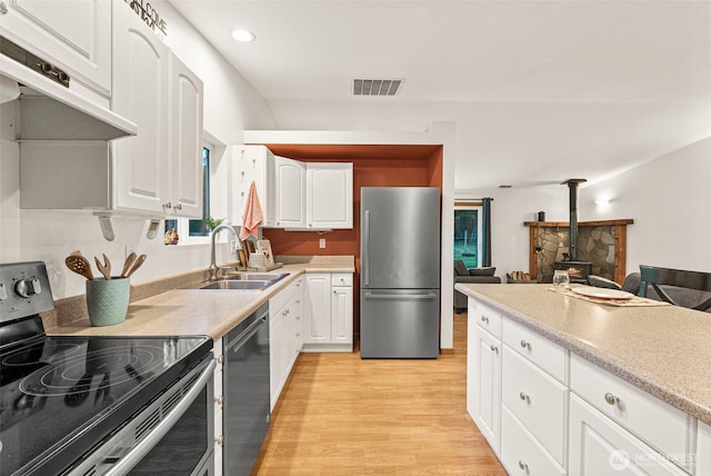 kitchen featuring visible vents, a wood stove, stainless steel appliances, under cabinet range hood, and a sink