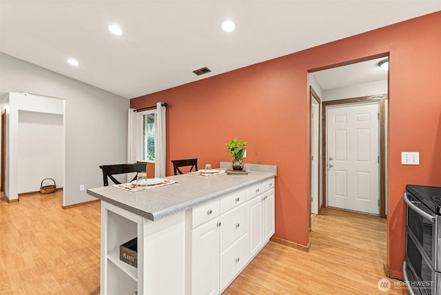 kitchen featuring light wood-type flooring, double oven range, white cabinets, and a peninsula