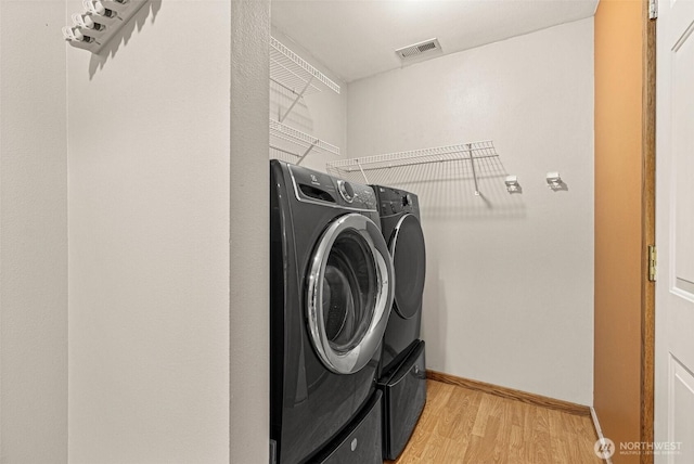 laundry area featuring laundry area, visible vents, baseboards, washer and clothes dryer, and light wood-type flooring