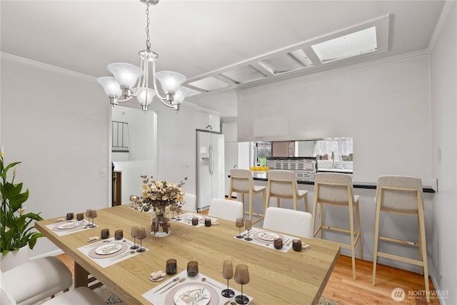 dining area with a notable chandelier, light wood-style flooring, and crown molding