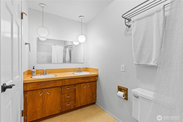 full bathroom with baseboards, a sink, toilet, and double vanity